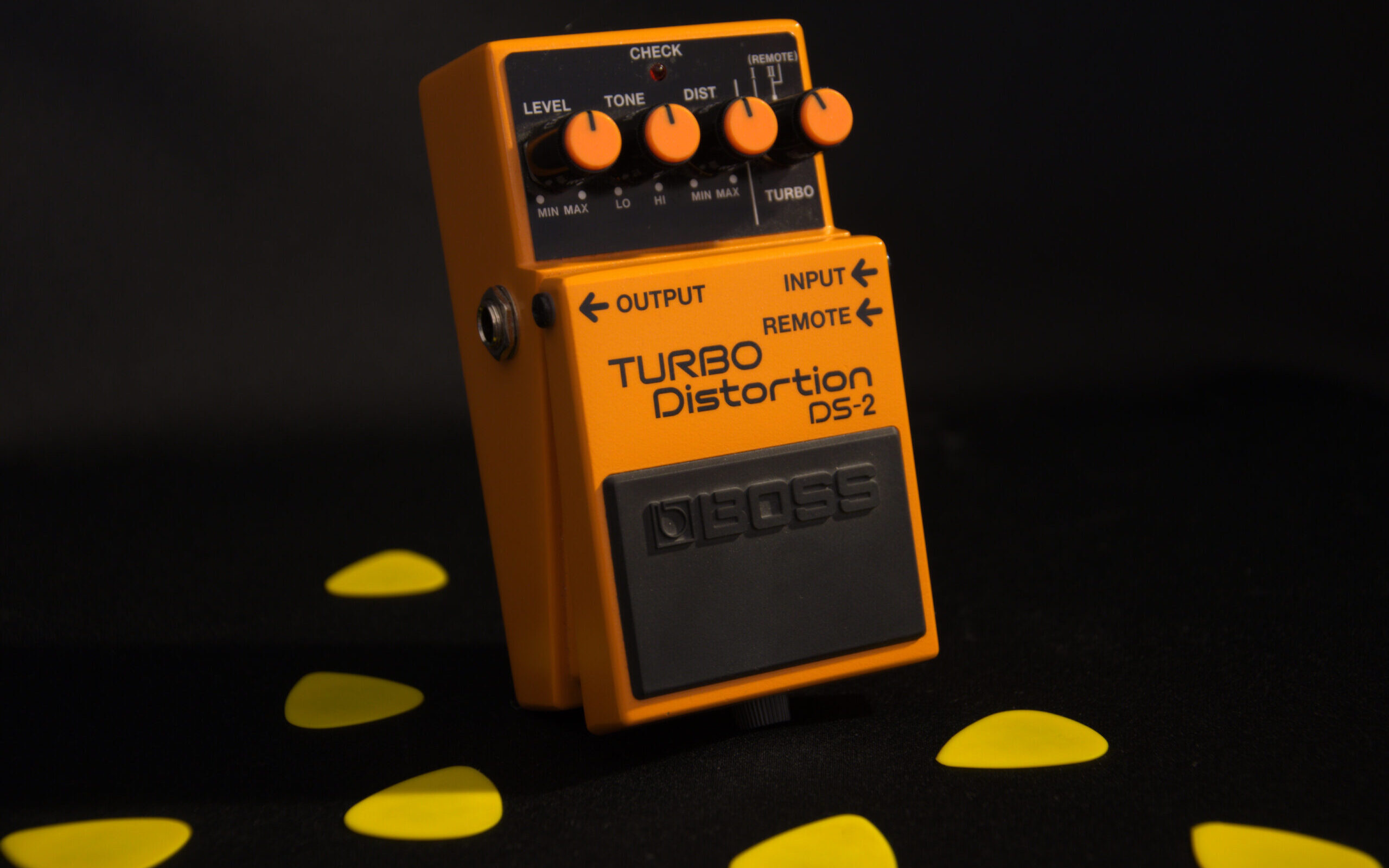 Guitar pedal on a black background next to guitar picks